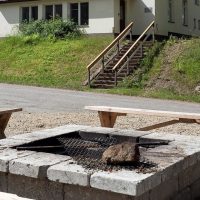 Kivistä rakennettu nuotiopaikka residenssitalon pihalla, taustalla näkyy portaat rakennuksen sisäänkäynnille.